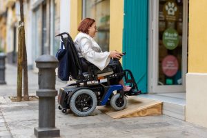 Electric wheelchair user successfully navigates a wooden ramp to access a store, demonstrating accessible architecture.