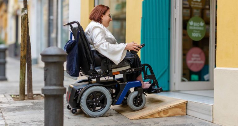 Electric wheelchair user successfully navigates a wooden ramp to access a store, demonstrating accessible architecture.